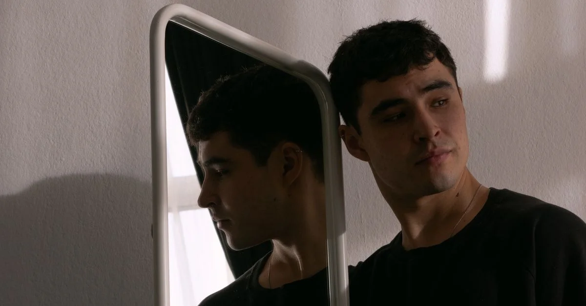 Joven mirando en un espejo, creando un ambiente introspectivo y reflexivo.