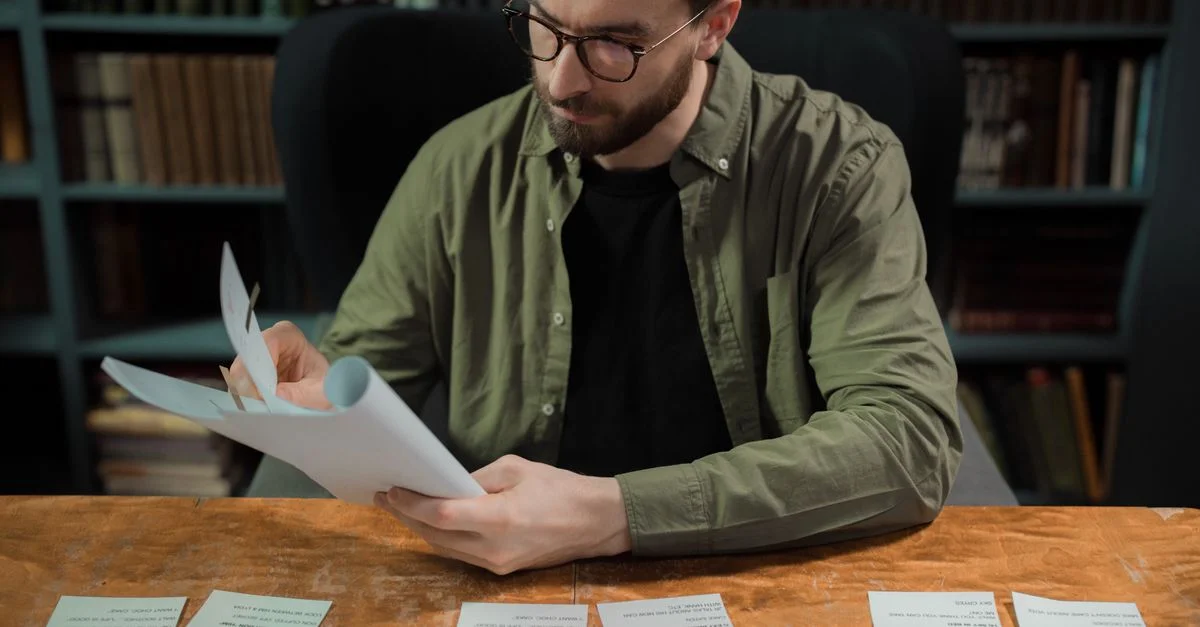 Hombre adulto estudiando papeles en un entorno de biblioteca, enfocado en educación e investigación.