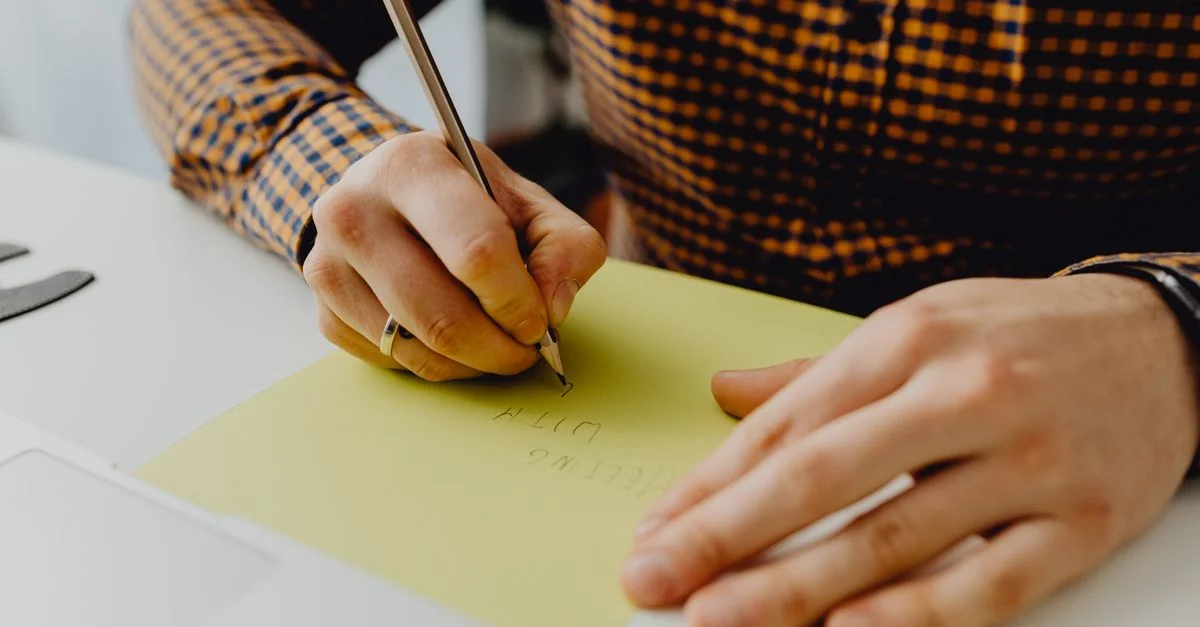 Una persona escribiendo en papel amarillo con un bolígrafo, capturando un momento de creatividad y expresión.