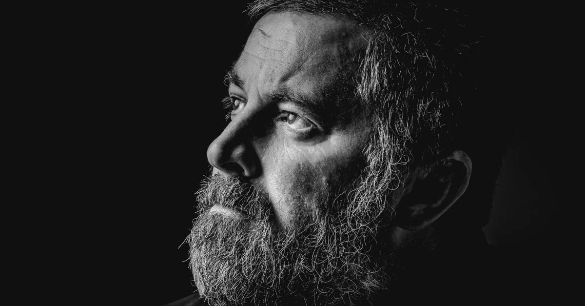 Retrato intenso en perfil lateral de un hombre con barba en iluminación monocromática.