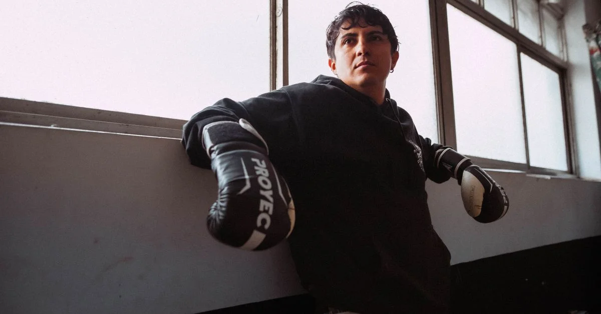 Un joven boxeador con ropa negra descansa en un gimnasio de Buenos Aires. Se aprecia una fuerte determinación.