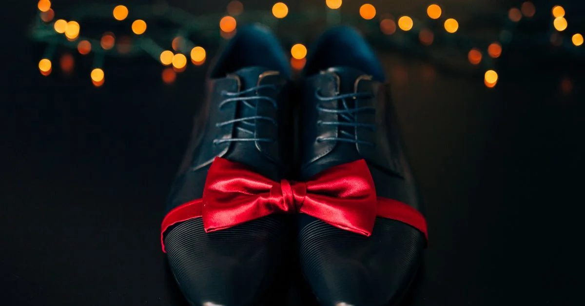 Zapatos de cuero negro elegantes adornados con una pajarita roja, ideales para ocasiones formales.