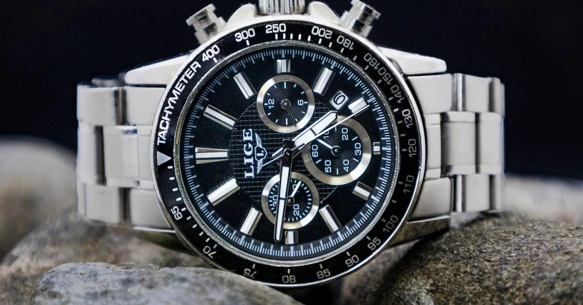 Primer plano de un elegante reloj plateado con múltiples esferas sobre rocas.